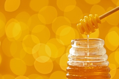 Honey pouring from dipper into jar on blurred background. Space for text