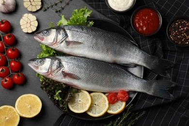 Photo of Fresh raw sea bass fish and ingredients on black table, flat lay