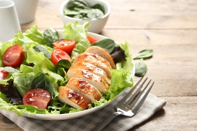 Photo of Eating delicious salad with chicken, cherry tomato and spinach served on wooden table, closeup. Space for text