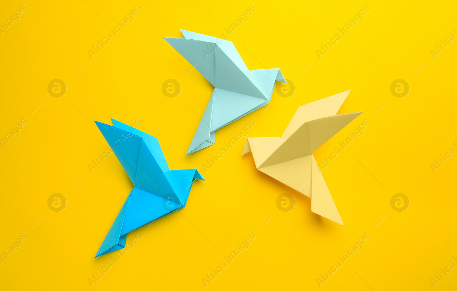 Photo of Origami art. Colorful handmade paper birds on yellow background, flat lay