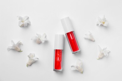 Bright lip glosses and flowers on white background, flat lay