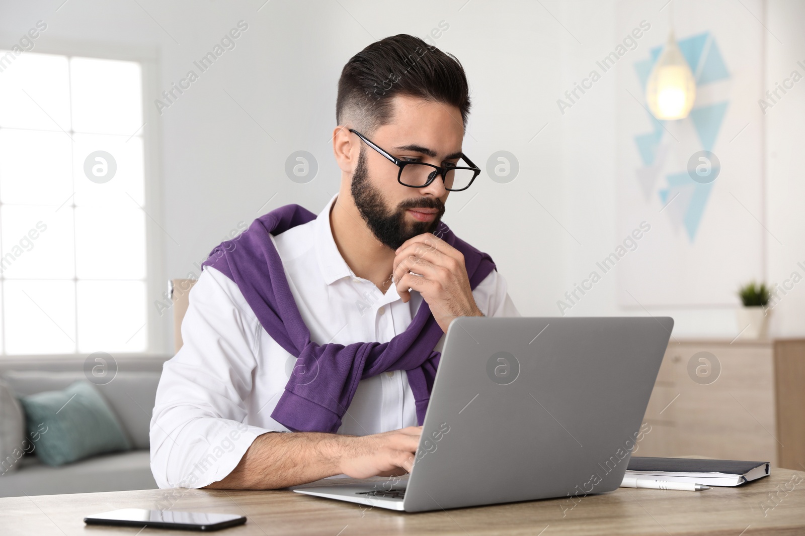 Photo of Handsome young man working with laptop at table in home office