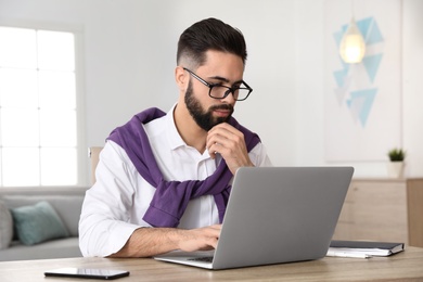 Handsome young man working with laptop at table in home office