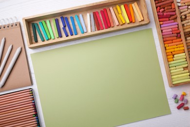 Photo of Layout with blank paper, soft pastels and other drawing supplies on white wooden table at artist's workplace, top view. Space for design