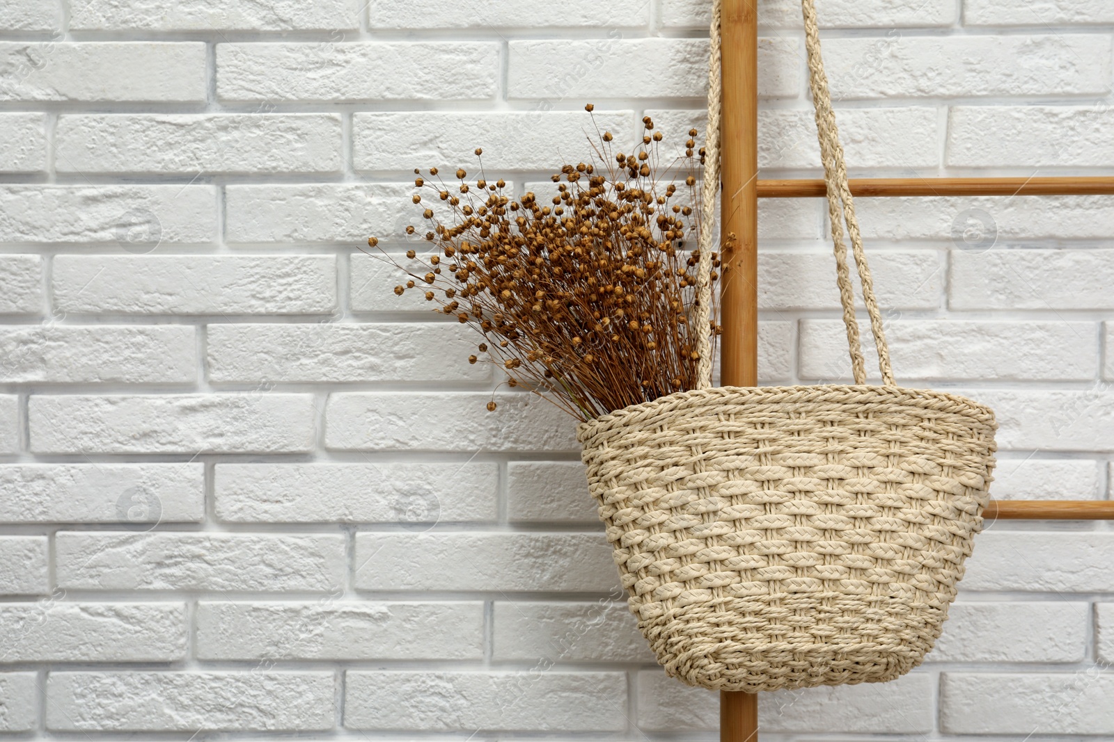 Photo of Stylish beach bag with beautiful dried flowers hanging  on wooden ladder. Space for text