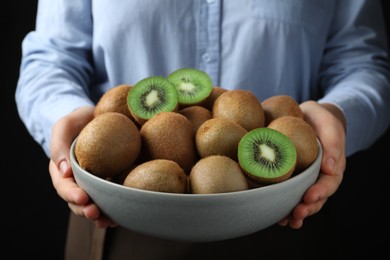 Woman holding bowl with fresh ripe kiwis on black background, closeup