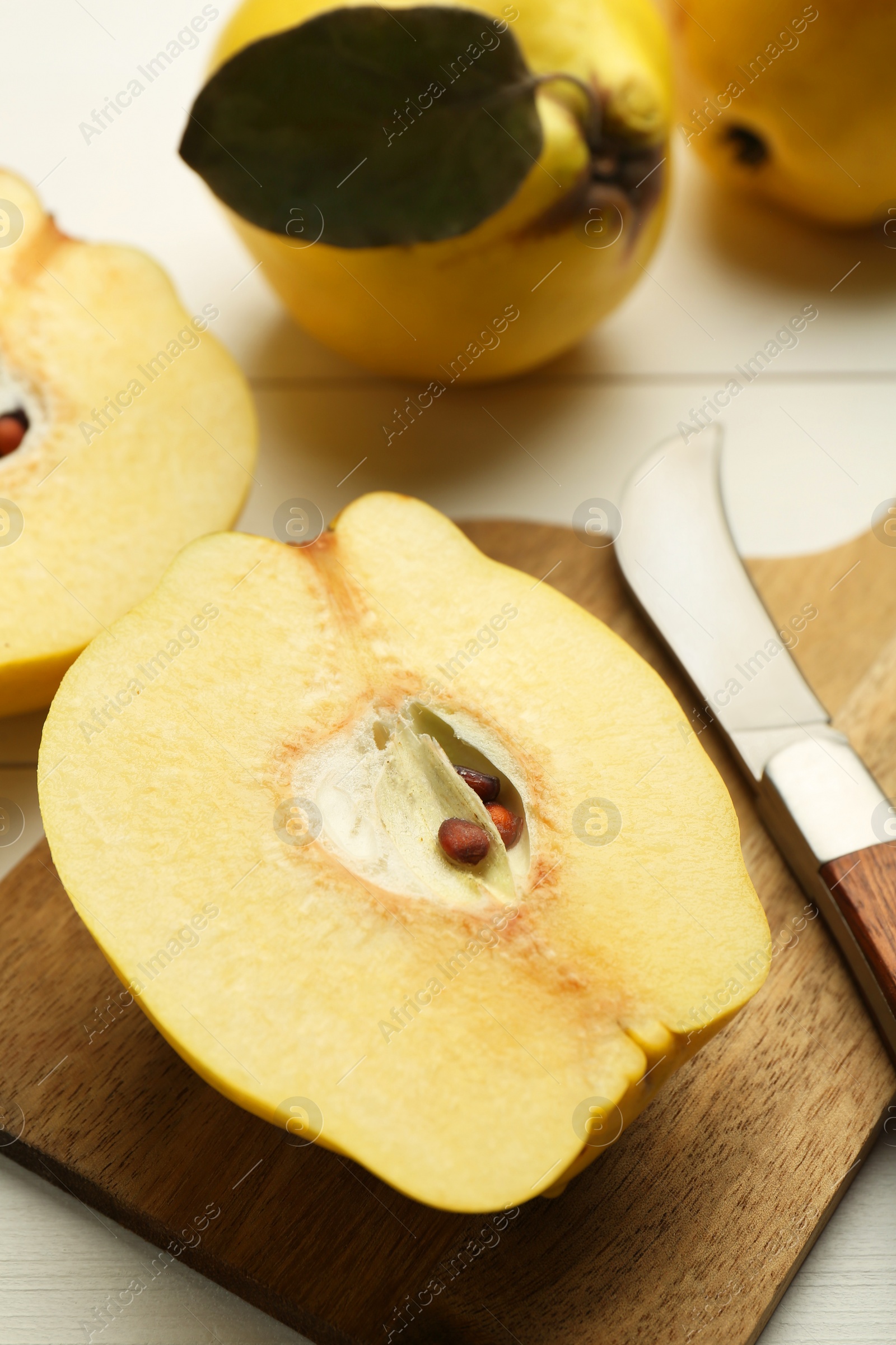 Photo of Tasty ripe quince fruits and knife on white wooden table, closeup