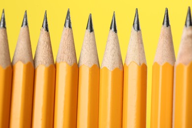 Photo of Many sharp graphite pencils on yellow background, macro view