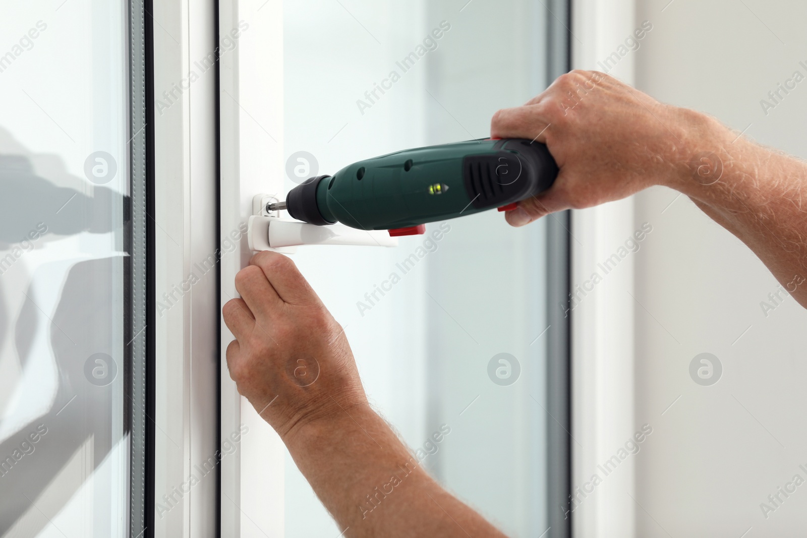 Photo of Construction worker repairing plastic window with electric screwdriver indoors, closeup