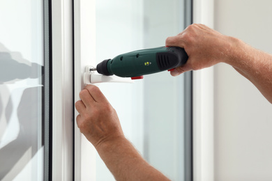 Construction worker repairing plastic window with electric screwdriver indoors, closeup