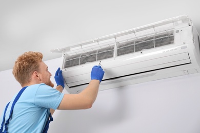 Professional technician maintaining modern air conditioner indoors