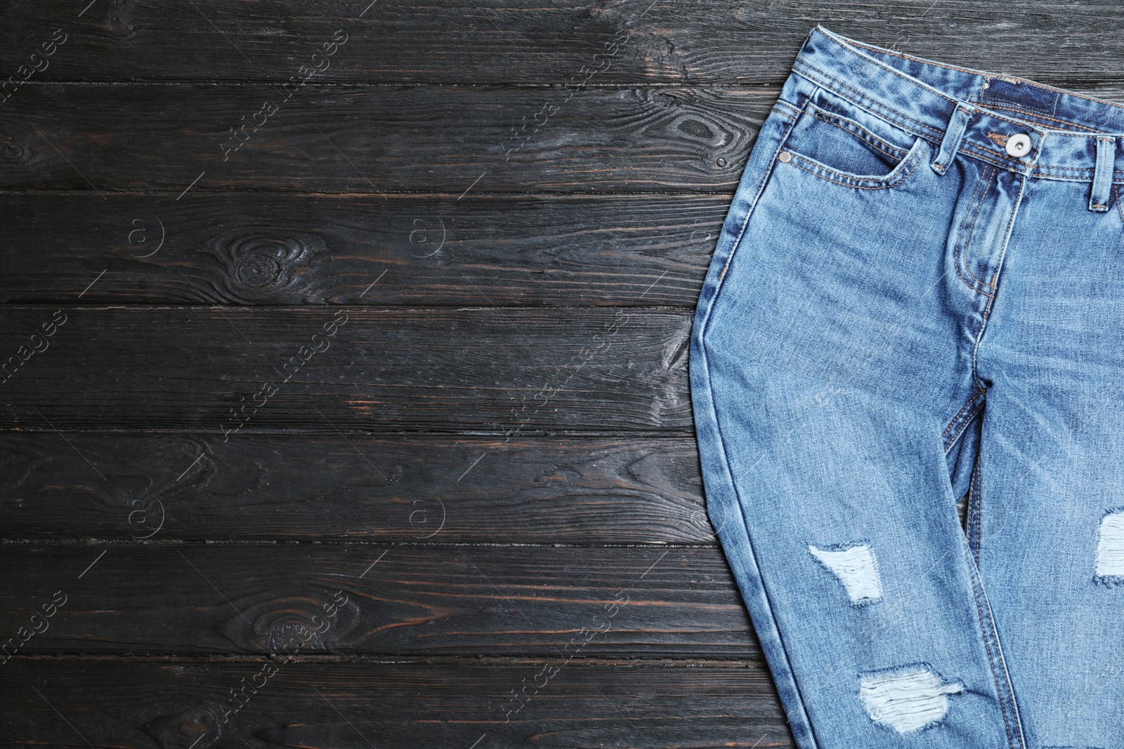 Photo of Stylish jeans on black wooden background, top view. Space for text