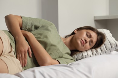 Photo of Young woman suffering from menstrual pain on bed at home