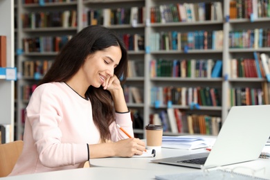 Photo of Young woman studying at table in library