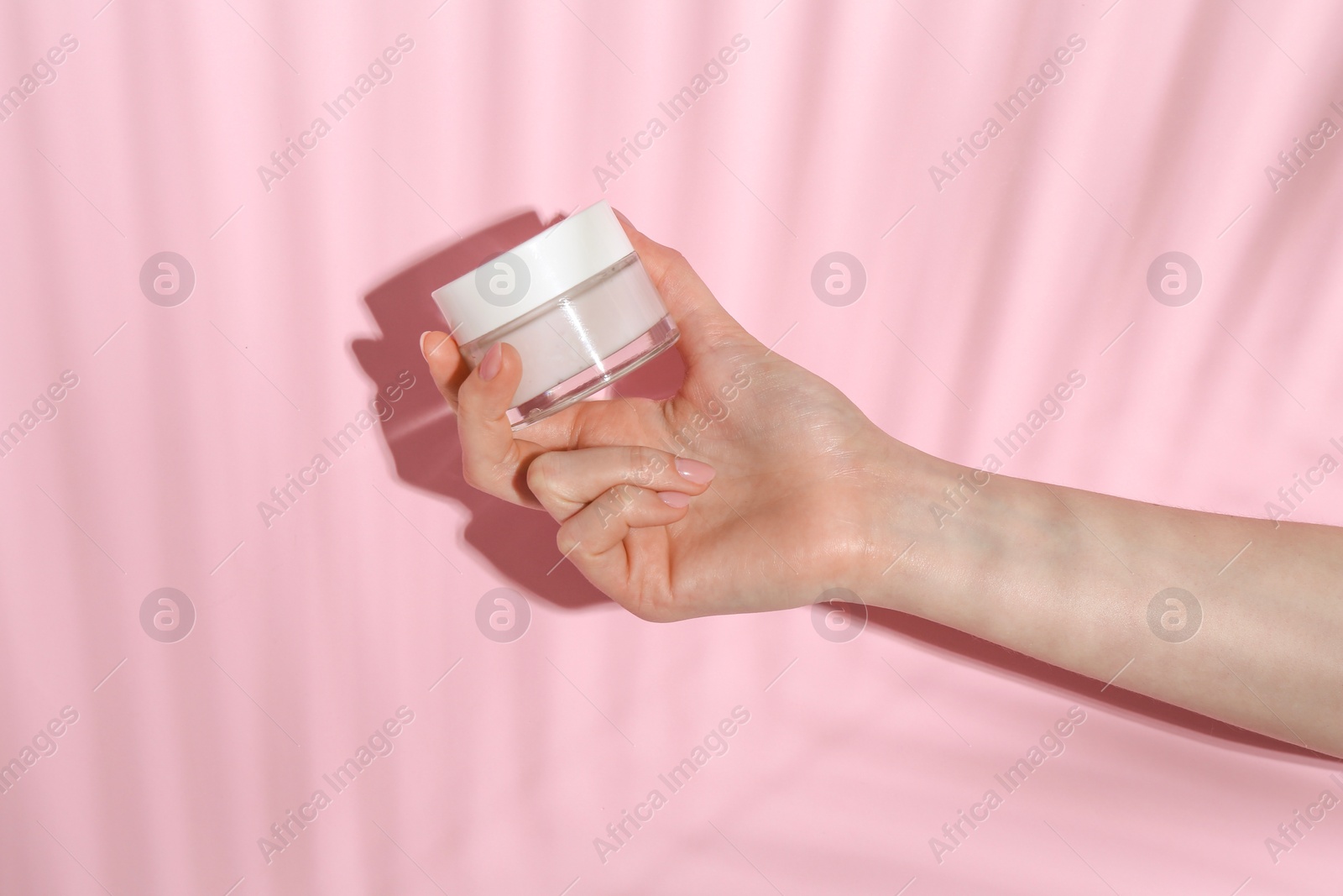 Photo of Woman holding jar of cream on pink background, closeup