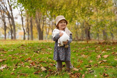 Girl walking with cute white rabbit in autumn park