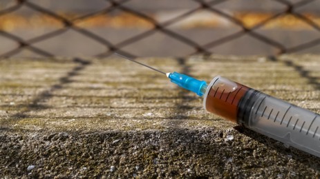 Photo of Syringe with hard drugs on stone surface outdoors, closeup. Space for text