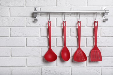 Photo of Rack with kitchen utensils hanging on white brick wall. Space for text