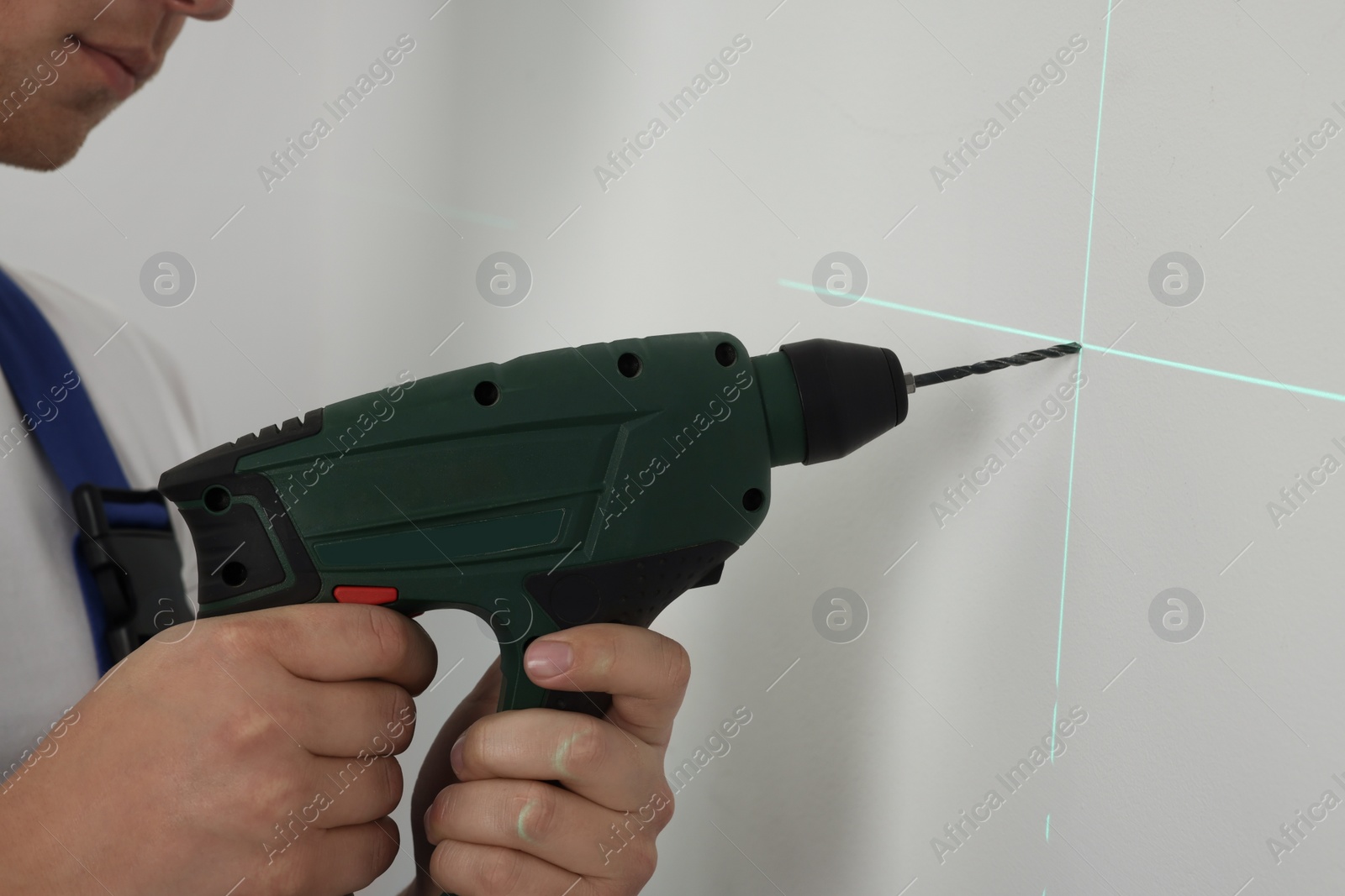 Photo of Man using cross line laser level for accurate measurement and drilling hole in light wall, closeup