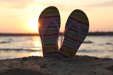 Photo of Stylish flip flops on sand near sea. Beach accessories