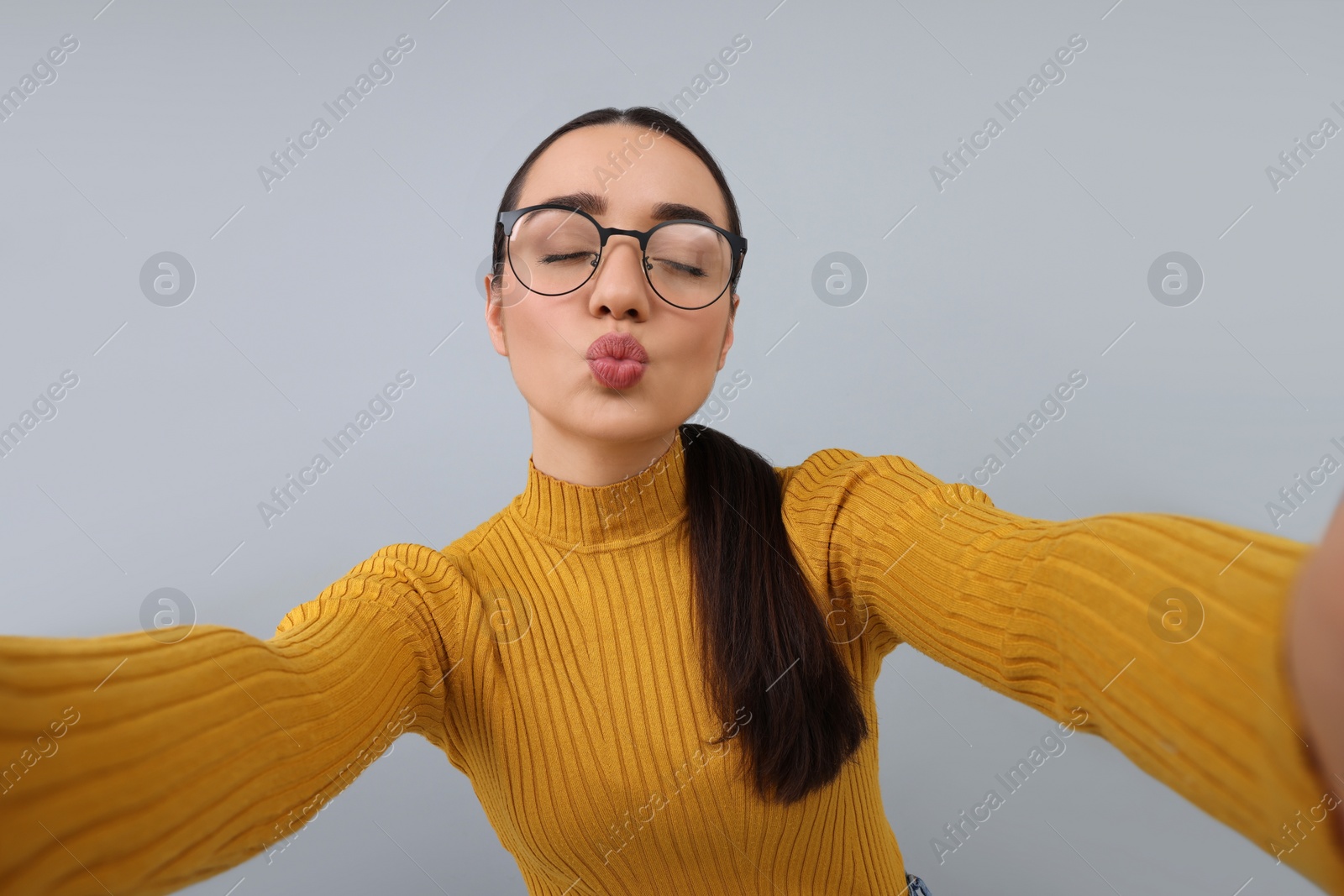 Photo of Young woman taking selfie and blowing kiss on grey background