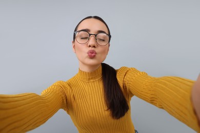 Young woman taking selfie and blowing kiss on grey background