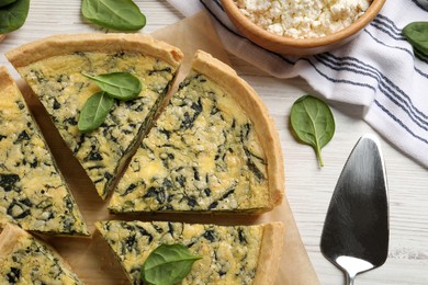 Cut delicious spinach pie with server on white wooden table, flat lay