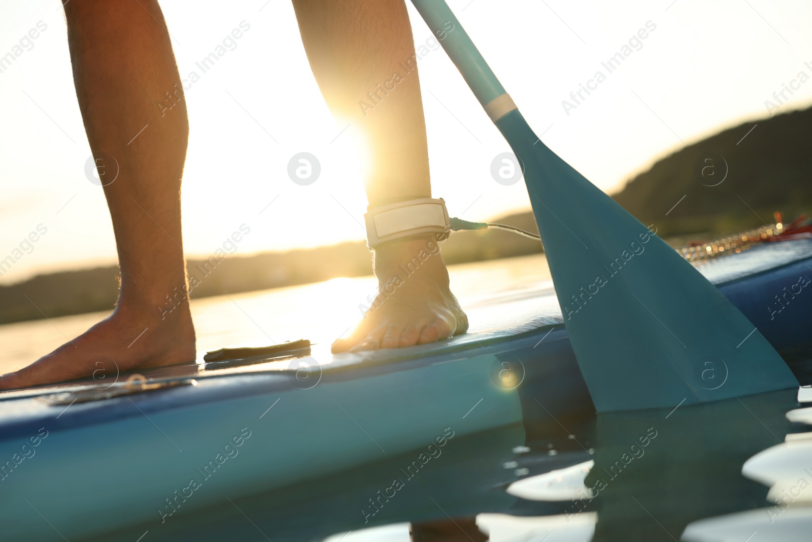 Photo of Man paddle boarding on SUP board in river at sunset, closeup