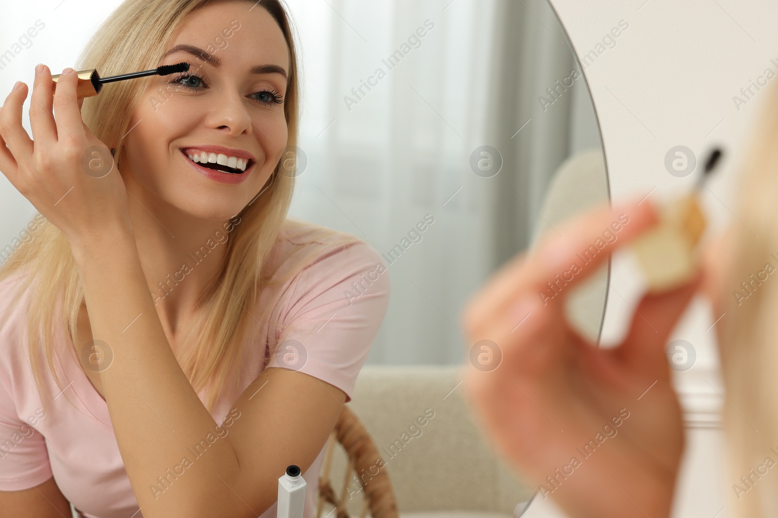 Photo of Beautiful woman applying mascara near mirror at home