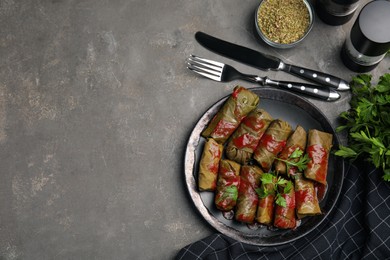 Photo of Delicious stuffed grape leaves with tomato sauce on grey table, flat lay. Space for text