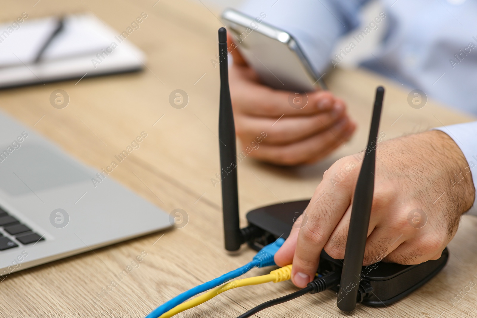 Photo of Man with smartphone and laptop connecting to internet via Wi-Fi router at wooden table, closeup