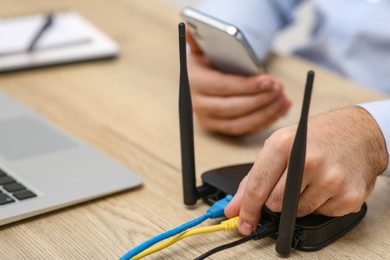 Photo of Man with smartphone and laptop connecting to internet via Wi-Fi router at wooden table, closeup