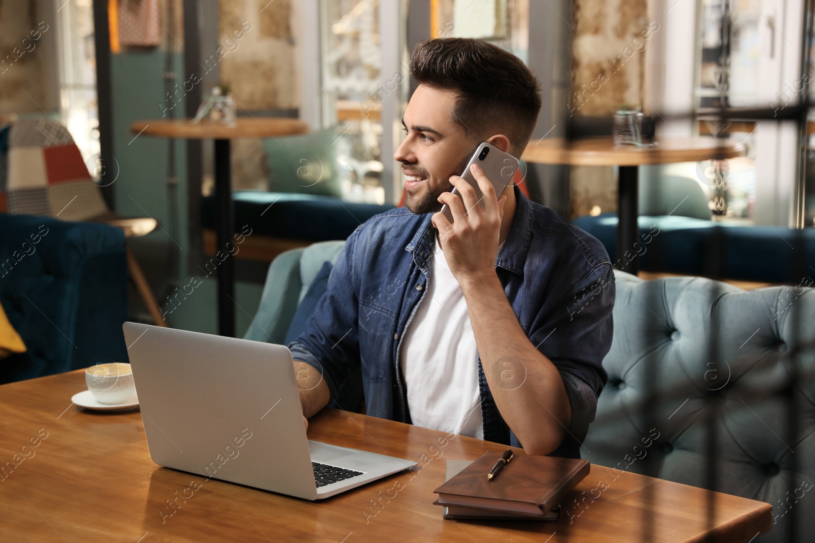 Photo of Young blogger talking on phone at table in cafe