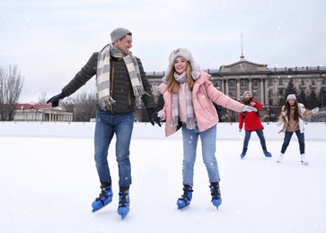 Image of Happy couple with friends skating along ice rink outdoors