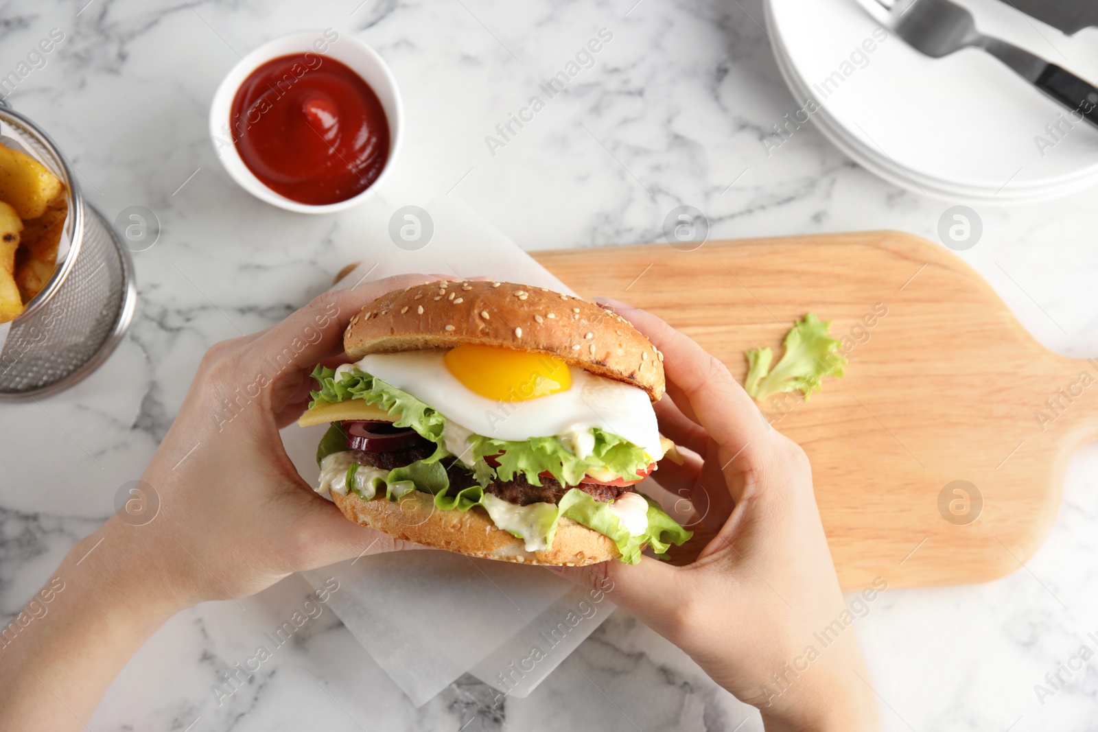 Photo of Woman holding tasty burger with fried egg over table, top view