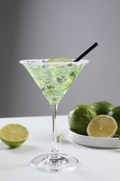 Photo of Delicious Margarita cocktail with ice cubes in glass and lime on white table