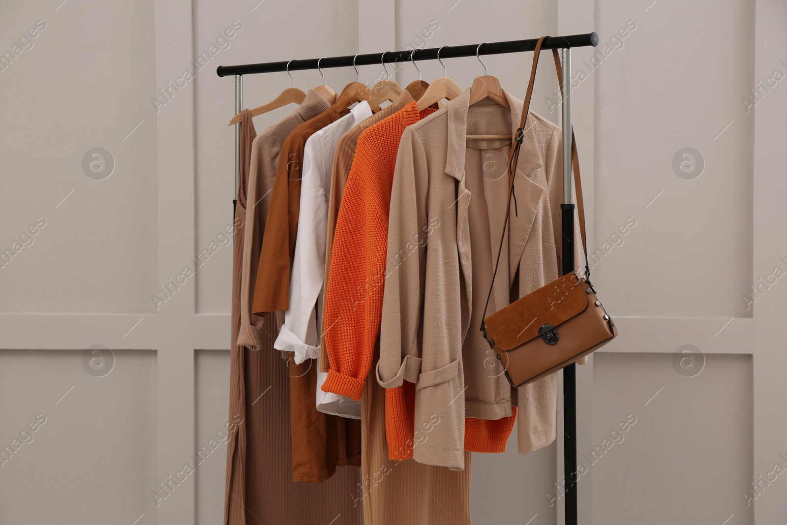 Photo of Rack with stylish women's clothes and bag near light wall