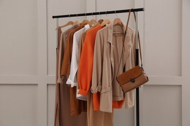 Photo of Rack with stylish women's clothes and bag near light wall