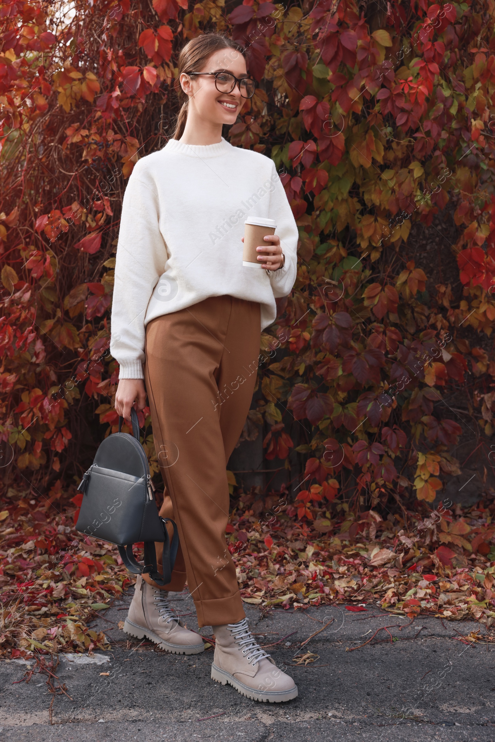 Photo of Beautiful young woman with stylish grey backpack and hot drink in autumn park