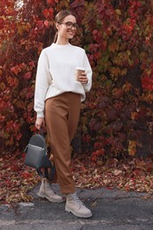 Photo of Beautiful young woman with stylish grey backpack and hot drink in autumn park