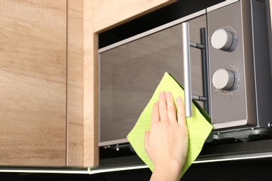 Photo of Woman cleaning microwave oven with rag in kitchen, closeup