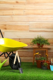Photo of Wheelbarrow with gardening tools and flowers near wooden wall. Space for text