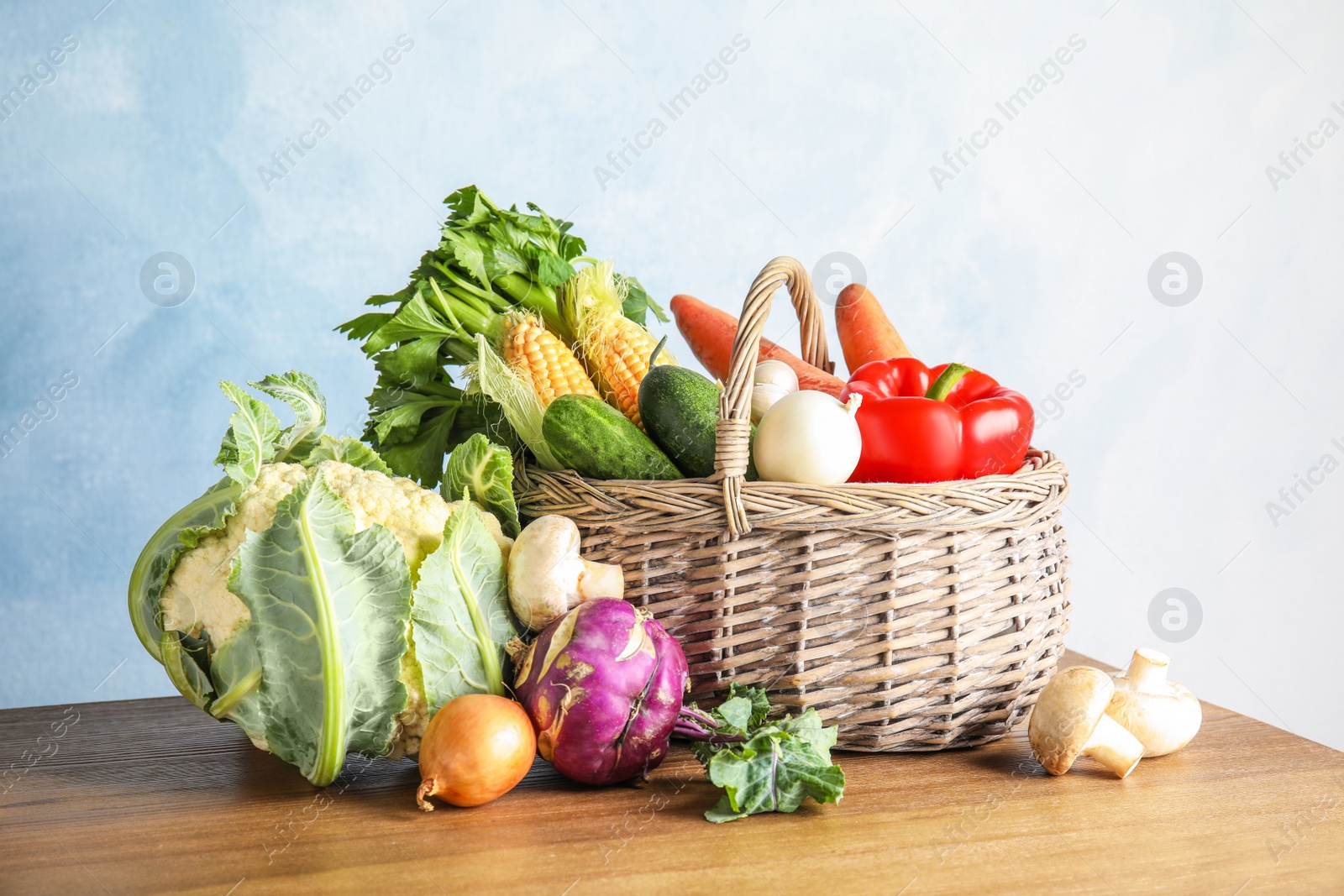 Photo of Basket full of fresh healthy vegetables on table against color background