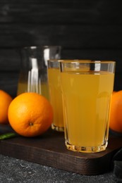 Photo of Many ripe oranges and fresh juice on dark grey table