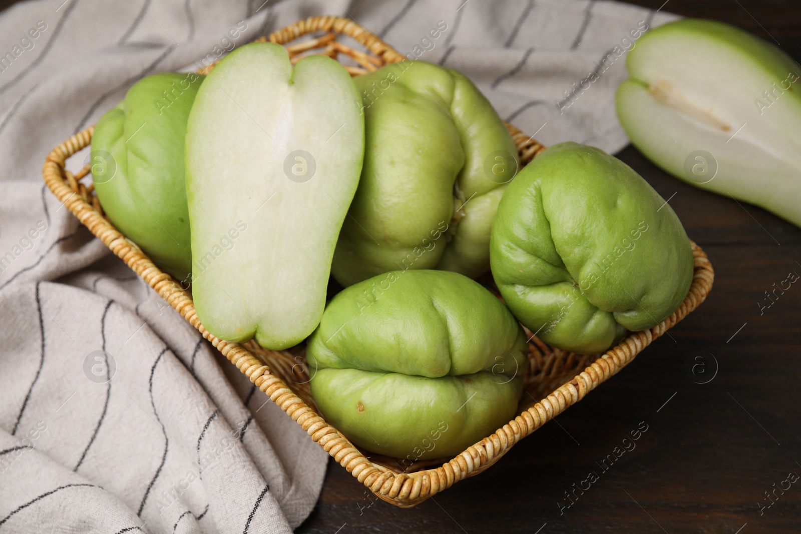 Photo of Cut and whole chayote in wicker basket on wooden table, above view
