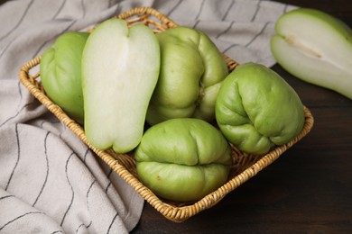 Cut and whole chayote in wicker basket on wooden table, above view