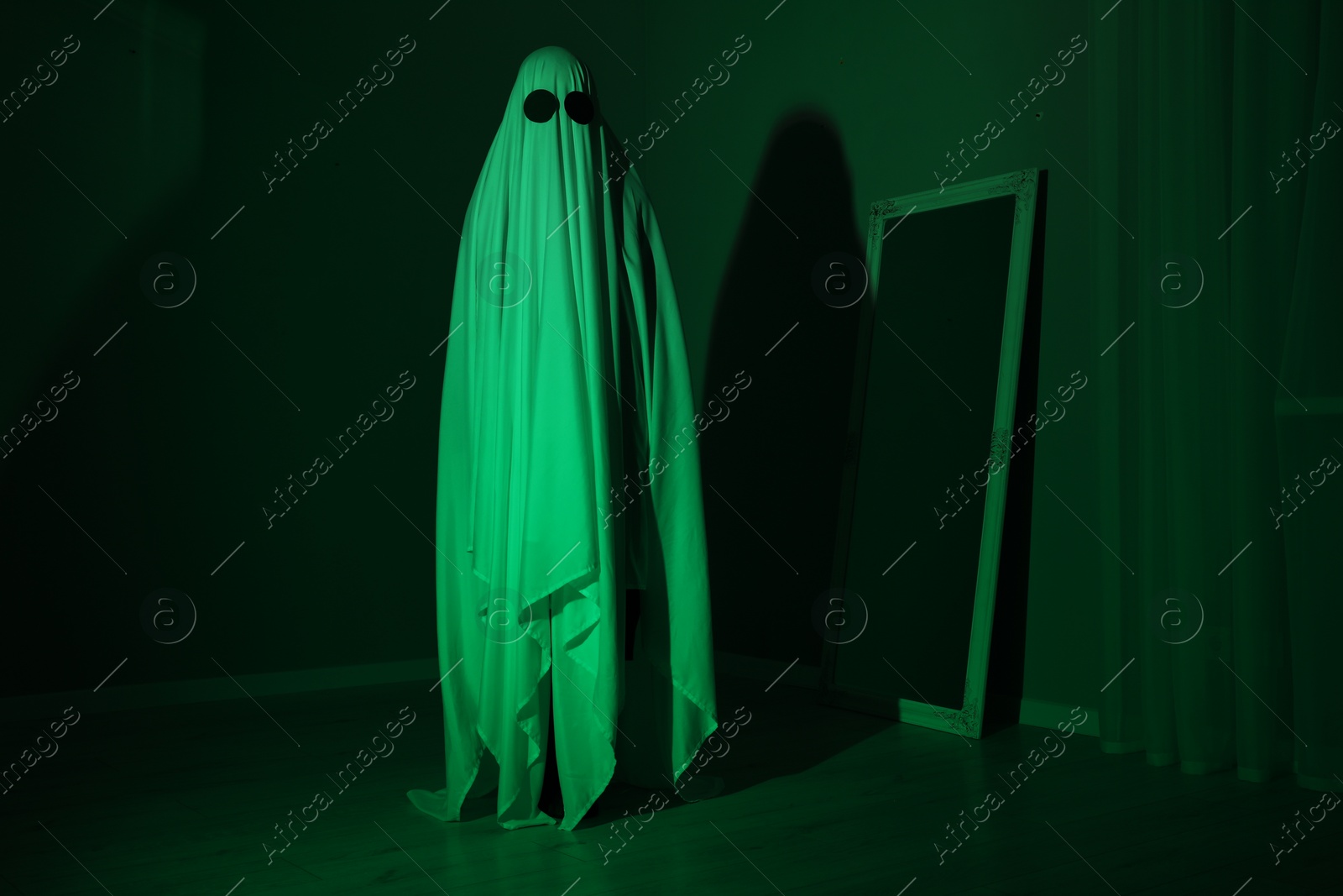 Photo of Creepy ghost. Woman covered with sheet in green light