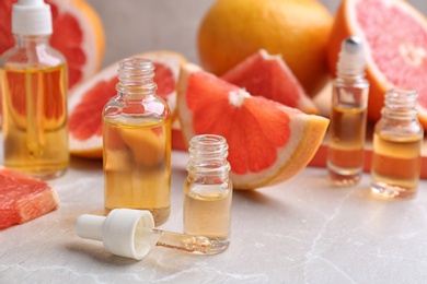 Bottles of essential oil and grapefruits on grey table, space for text