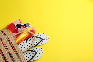 Bag with beach accessories on yellow background, flat lay. Space for text