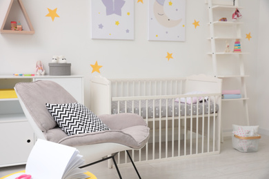 Photo of Stylish baby room interior with crib and armchair